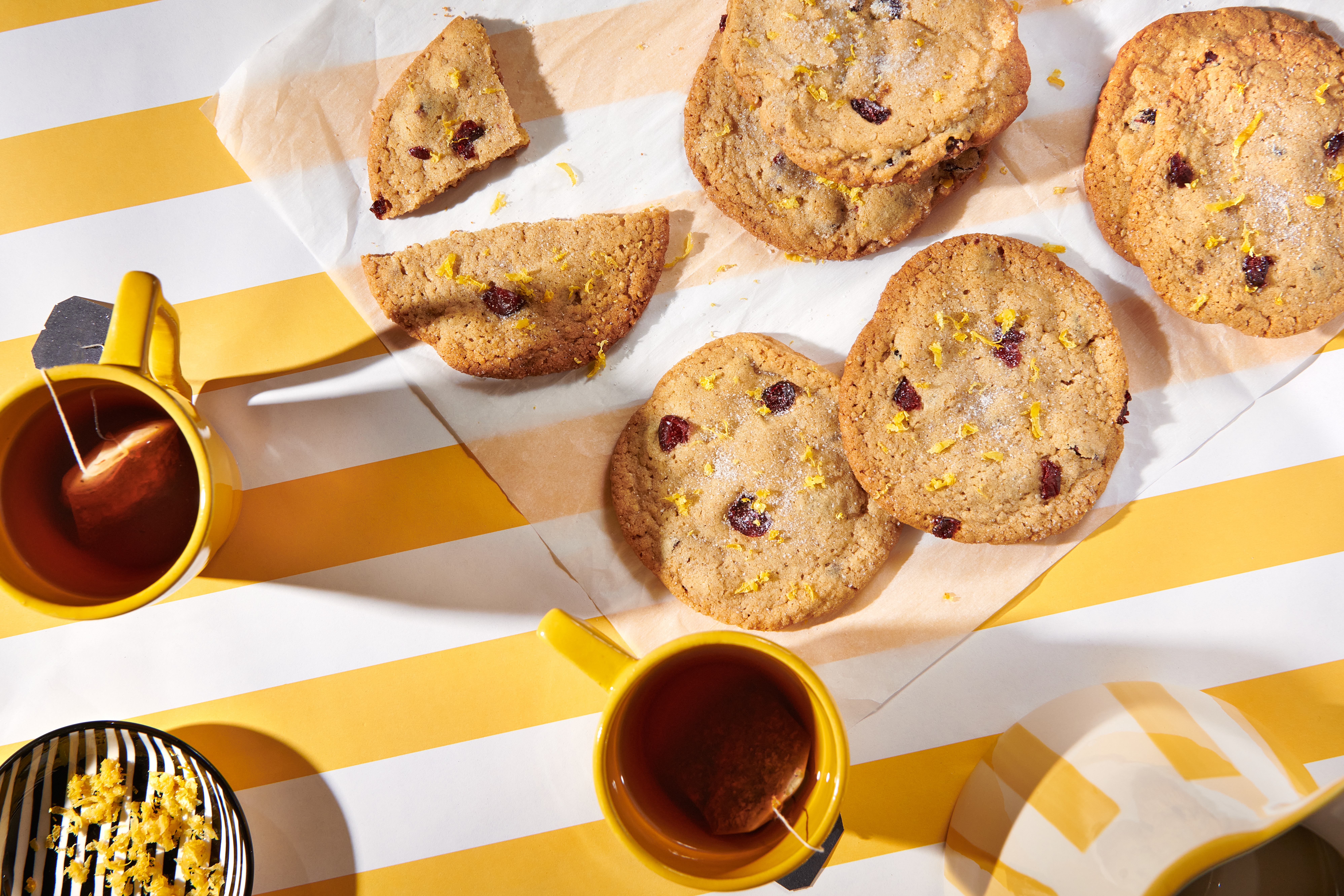 A tray of sesame cherry cookies set on a yellow-and-white striped tablecloth with cups of tea.